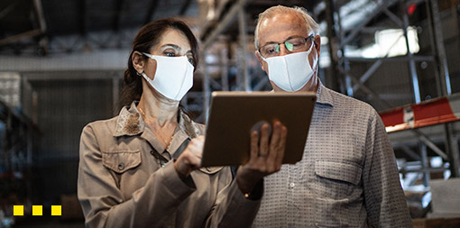 ey-man-and-woman-using-digital-tablet-in-warehouse-wearing-masks