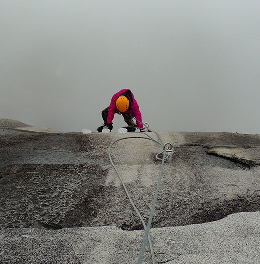 man climbing up cliff on rope in fog